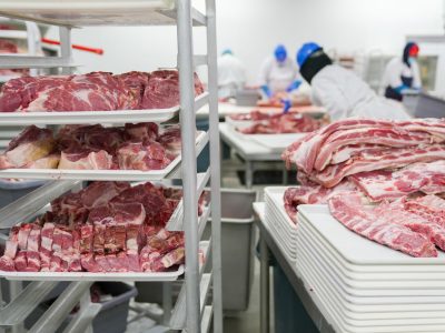 Trabalhadores manuseiam cortes de carne em uma unidade industrial de processamento de alimentos.