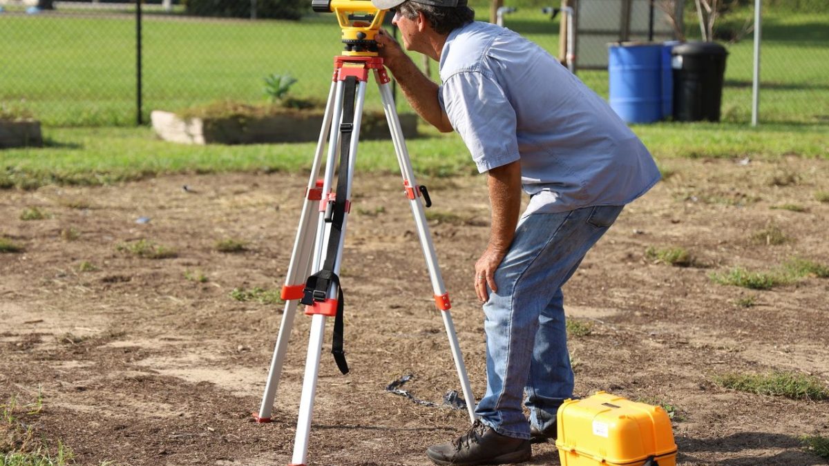 Profissional realiza medições com equipamento topográfico em uma área rural.