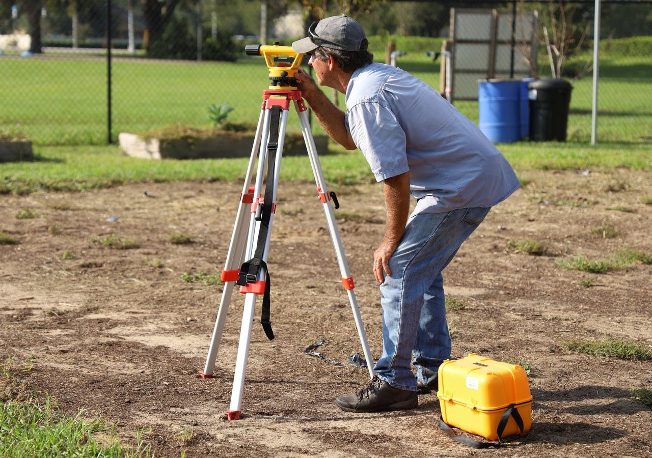 Profissional realiza medições com equipamento topográfico em uma área rural.