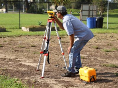 Profissional realiza medições com equipamento topográfico em uma área rural.