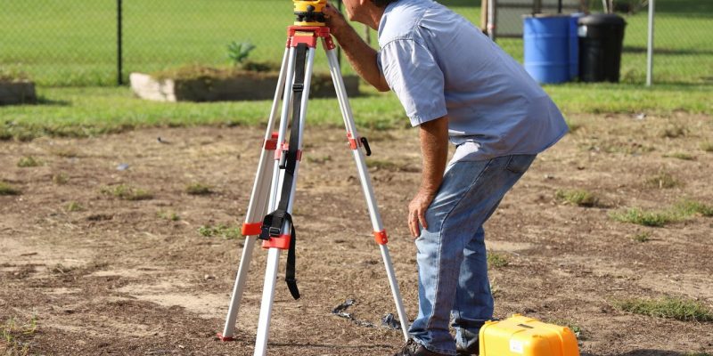 Profissional realiza medições com equipamento topográfico em uma área rural.